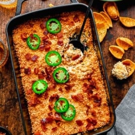 Overhead of jalapeno popper dip with a scoop taken out of it. A bowl of chips sits close by.