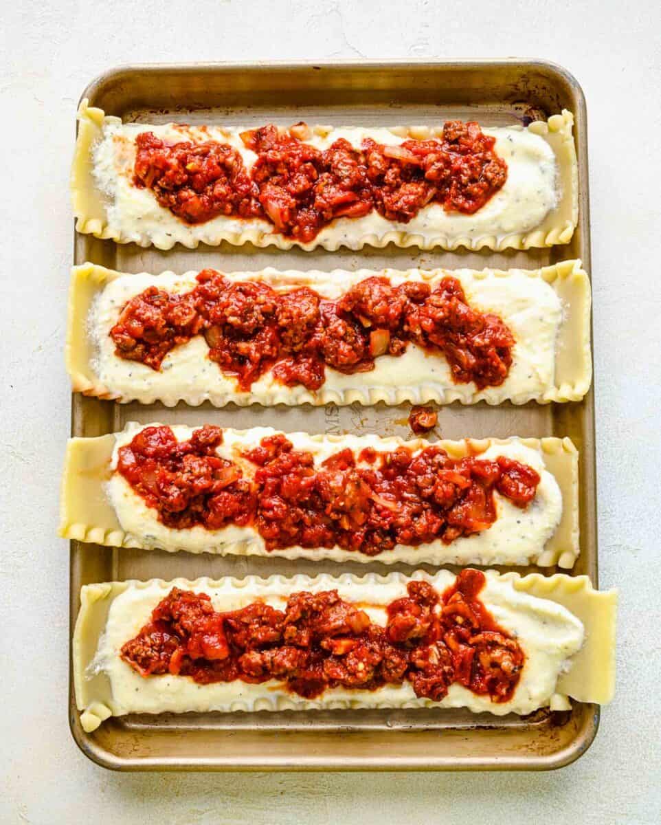 Spreading meat sauce over ricotta filling on lasagna noodles.