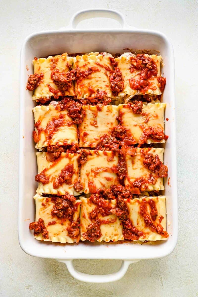 Spreading sauce over the top of lasagna roll ups in a baking pan.