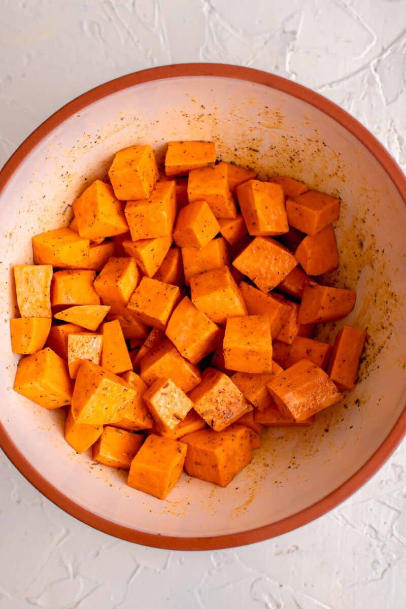 cubed sweet potatoes in a ceramic bowl with seasonings on top