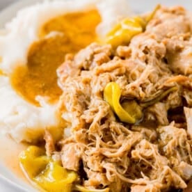 mississippi chicken with pepperoncinis on a plate with mashed potatoes and gravy next to the chicken