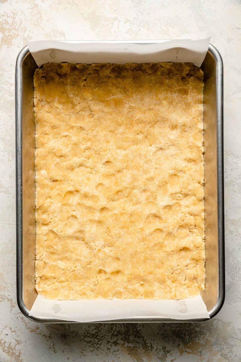 dough is pressed all along the bottom of a pan lined with parchment paper
