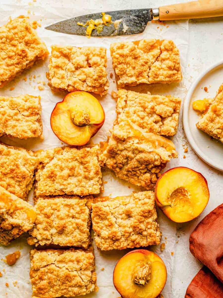 a large serving of sliced dessert bars are placed next to halved peaches