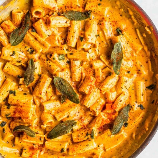 rigatoni pasta in a creamy pumpkin sauce in a large metal skillet topped with sage and fresh paprika and ground black pepper sprinkled on top