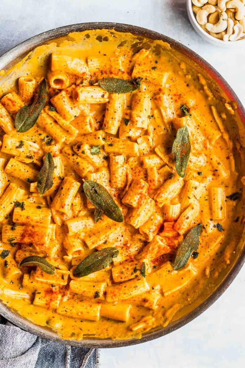 rigatoni pasta in a creamy pumpkin sauce in a large metal skillet topped with sage and fresh paprika and ground black pepper sprinkled on top