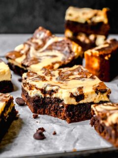 Cream cheese swirl brownies scattered on a surface. One has a bite taken out of it.