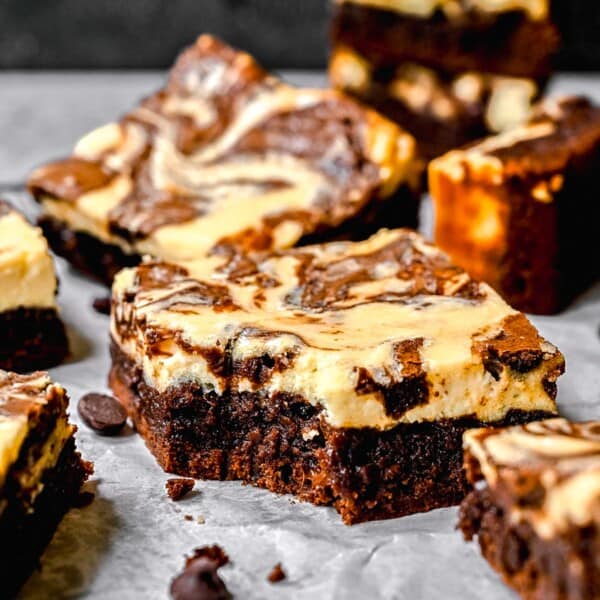 Cream cheese swirl brownies scattered on a surface. One has a bite taken out of it.