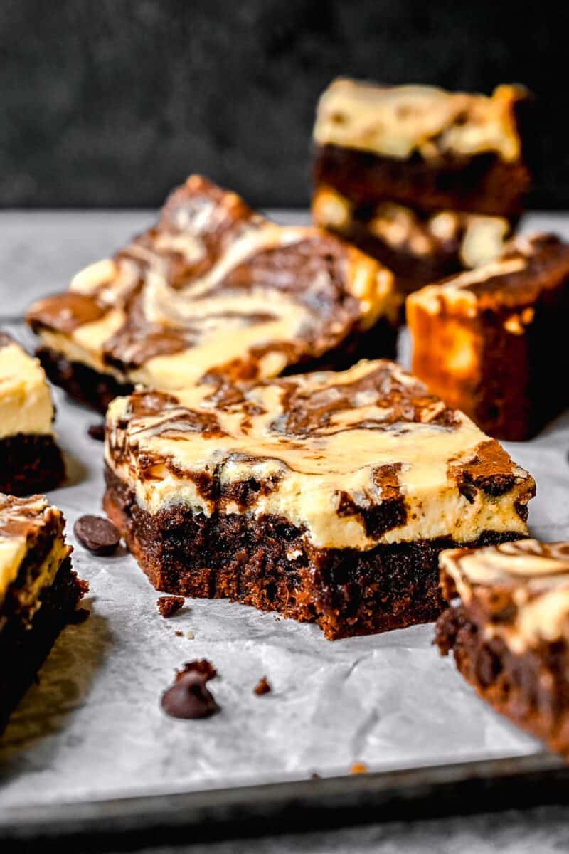 Cream cheese swirl brownies scattered on a surface. One has a bite taken out of it.