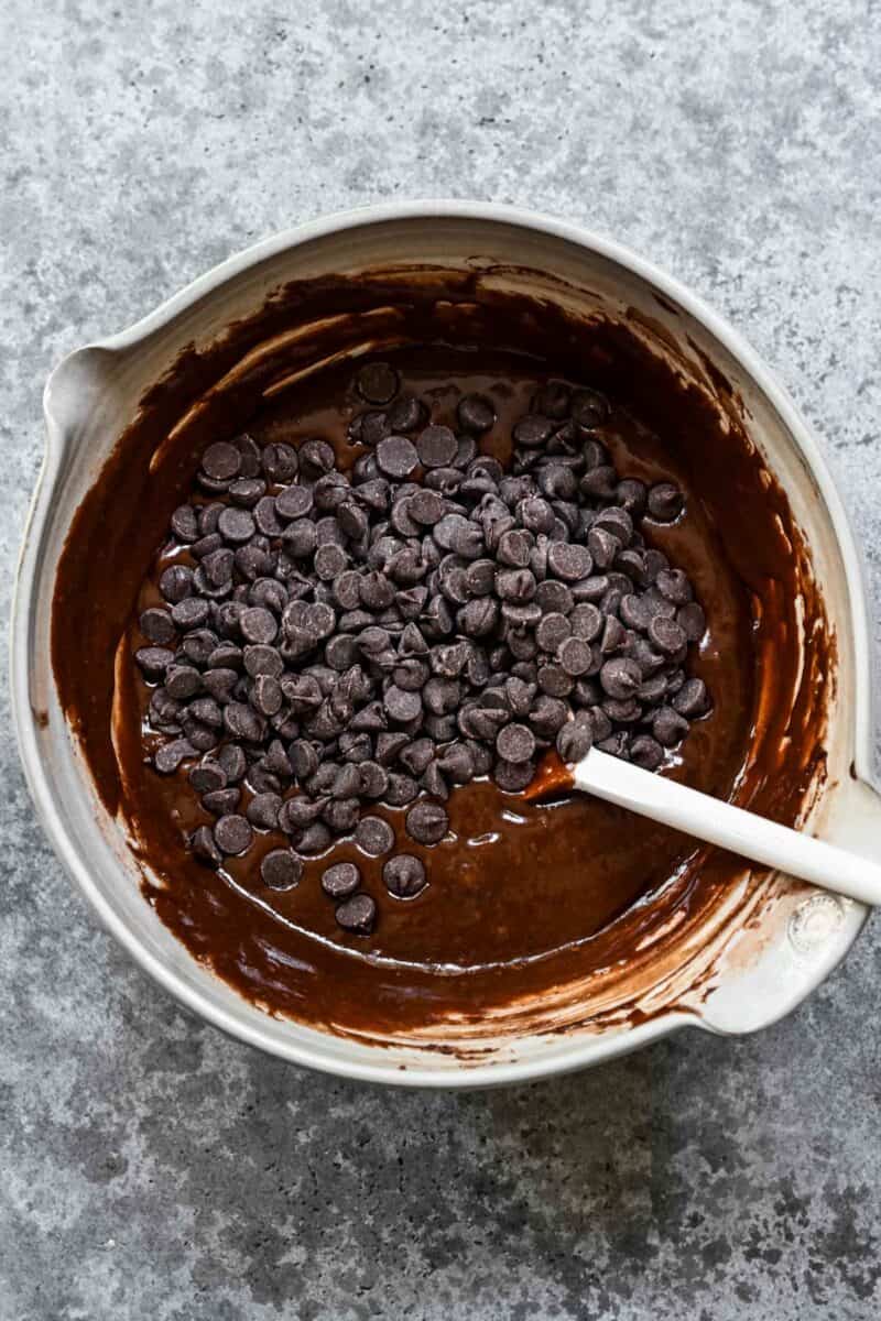 Adding chocolate chips to brownie batter in a mixing bowl.