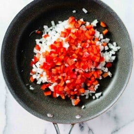diced onions and red bell peppers in a grey nonstick skillet with oil