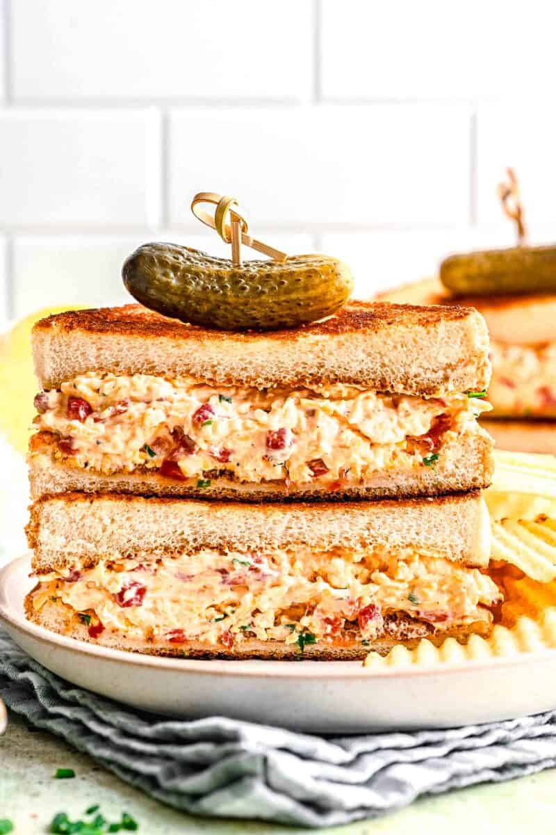 pimento cheese sandwich halves stacked on top of each other with a cornichon on top