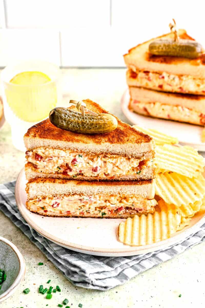 pimento cheese sandwich halves stacked on top of each other on a plate next to ruffled chips