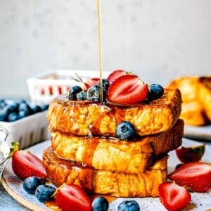 syrup being poured onto pumpkin french toast with fresh strawberries and blueberries on top