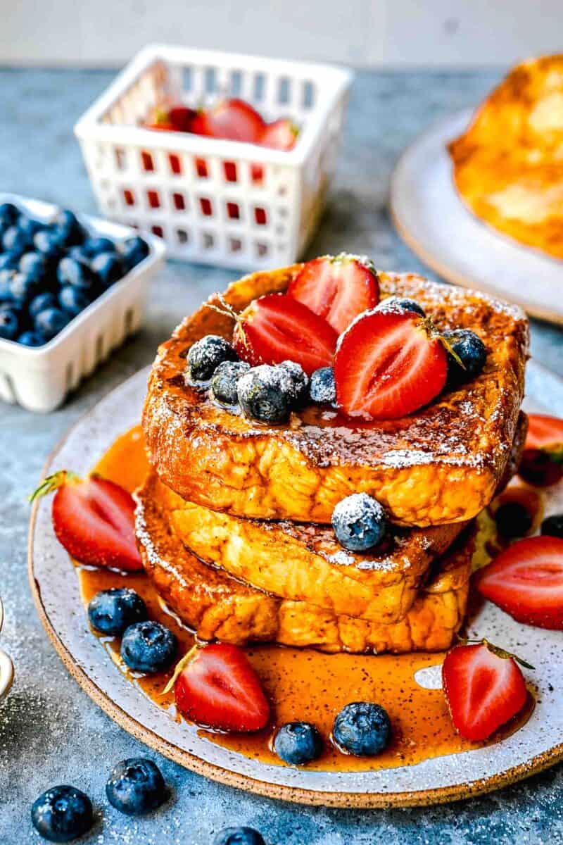 pumpkin french toast drizzled with syrup with fresh strawberries and blueberries on top