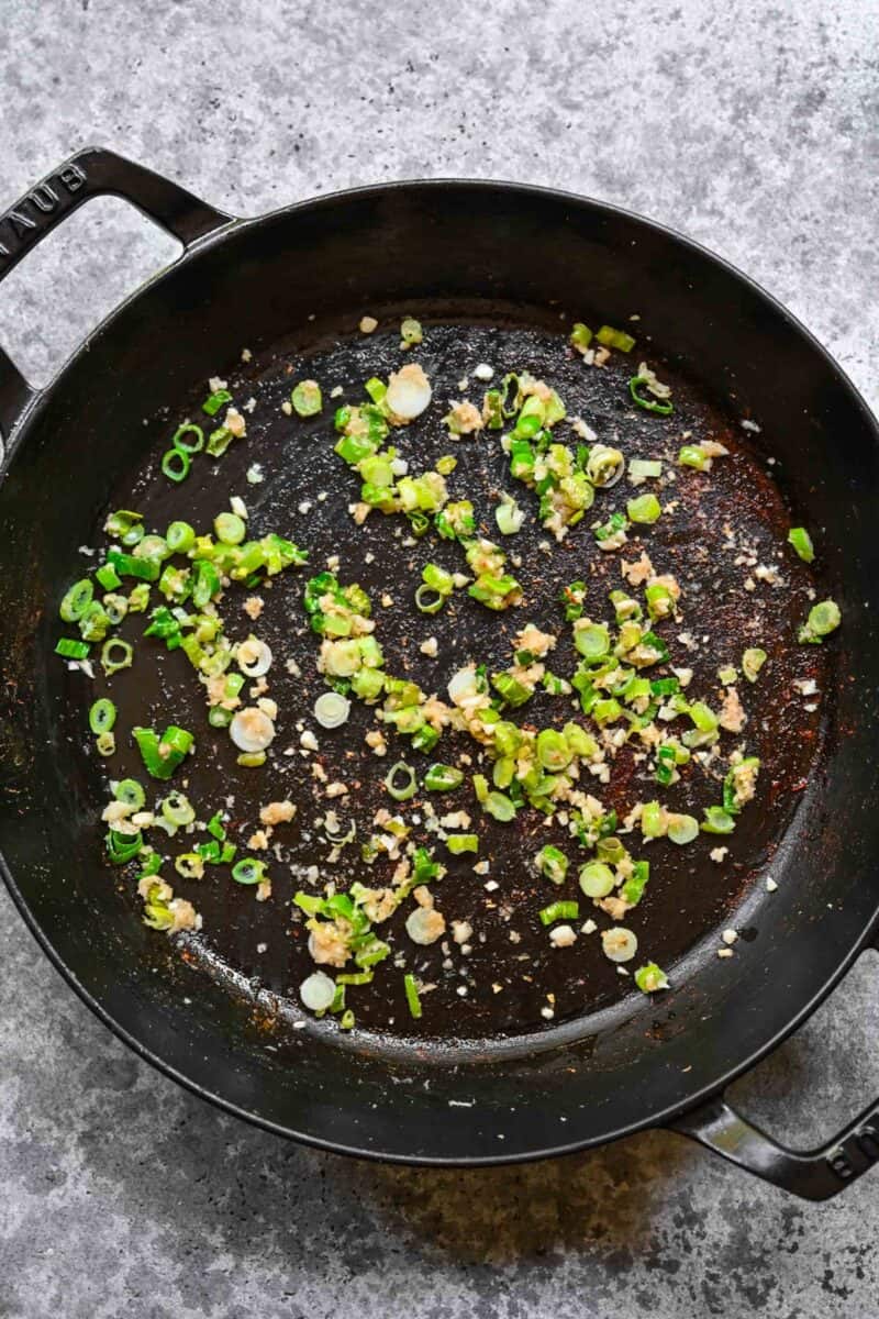 Sautéing garlic, ginger, and scallions in sesame oil in a skillet.