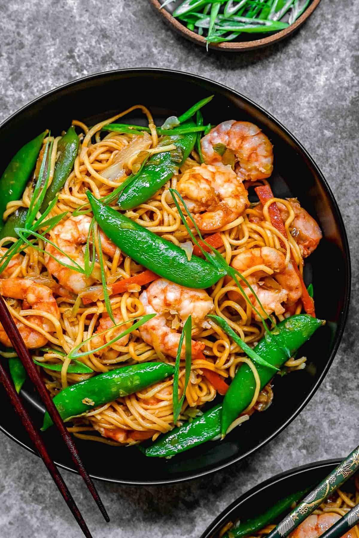 Closeup of shrimp chow mein served in a bowl with chopsticks.