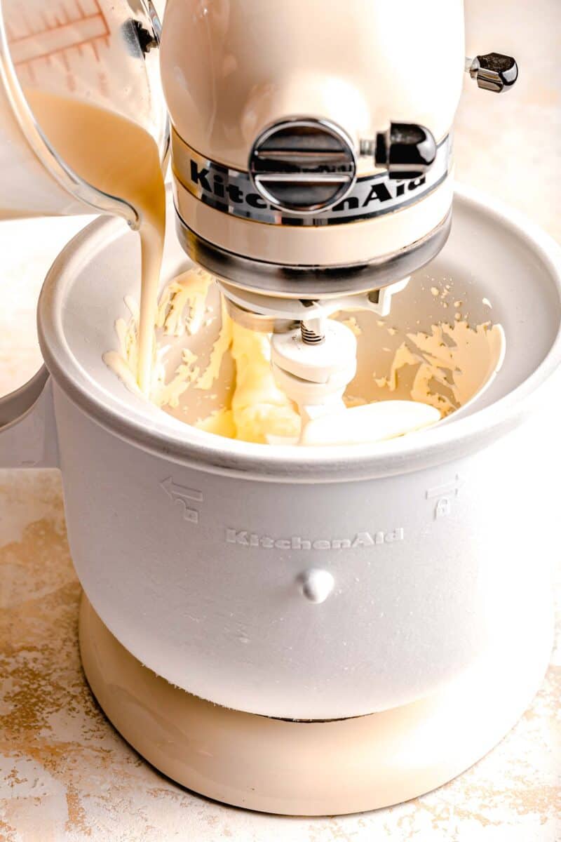 Pouring a mixture of heavy cream and sweetened condensed milk into the bowl of an ice cream maker.