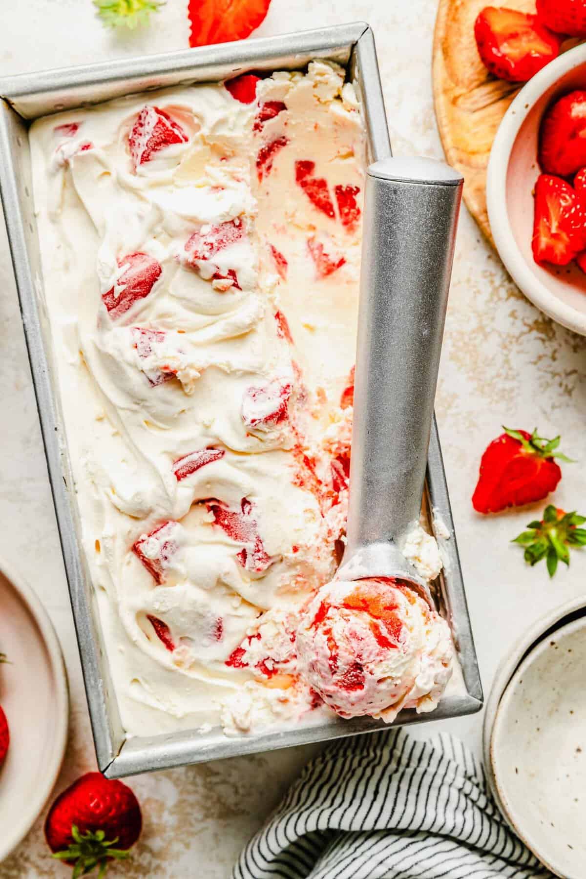 Taking a scoop of homemade strawberry ice cream out of a loaf pan.