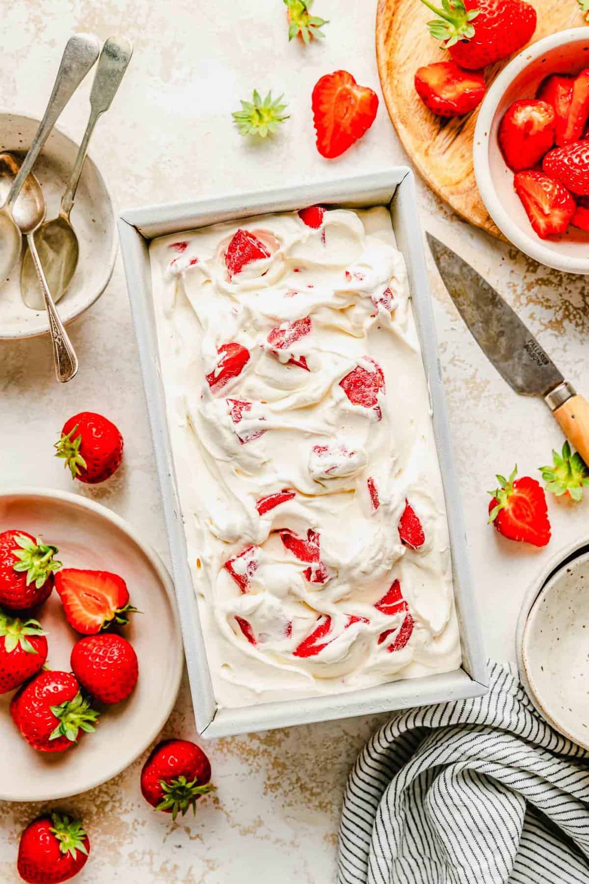 Homemade strawberry ice cream in a loaf pan surrounded by fresh strawberries.