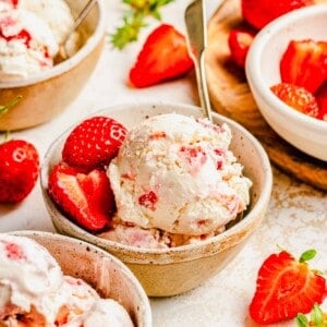 Strawberry ice cream served in bowls with spoons and garnished with fresh strawberries.