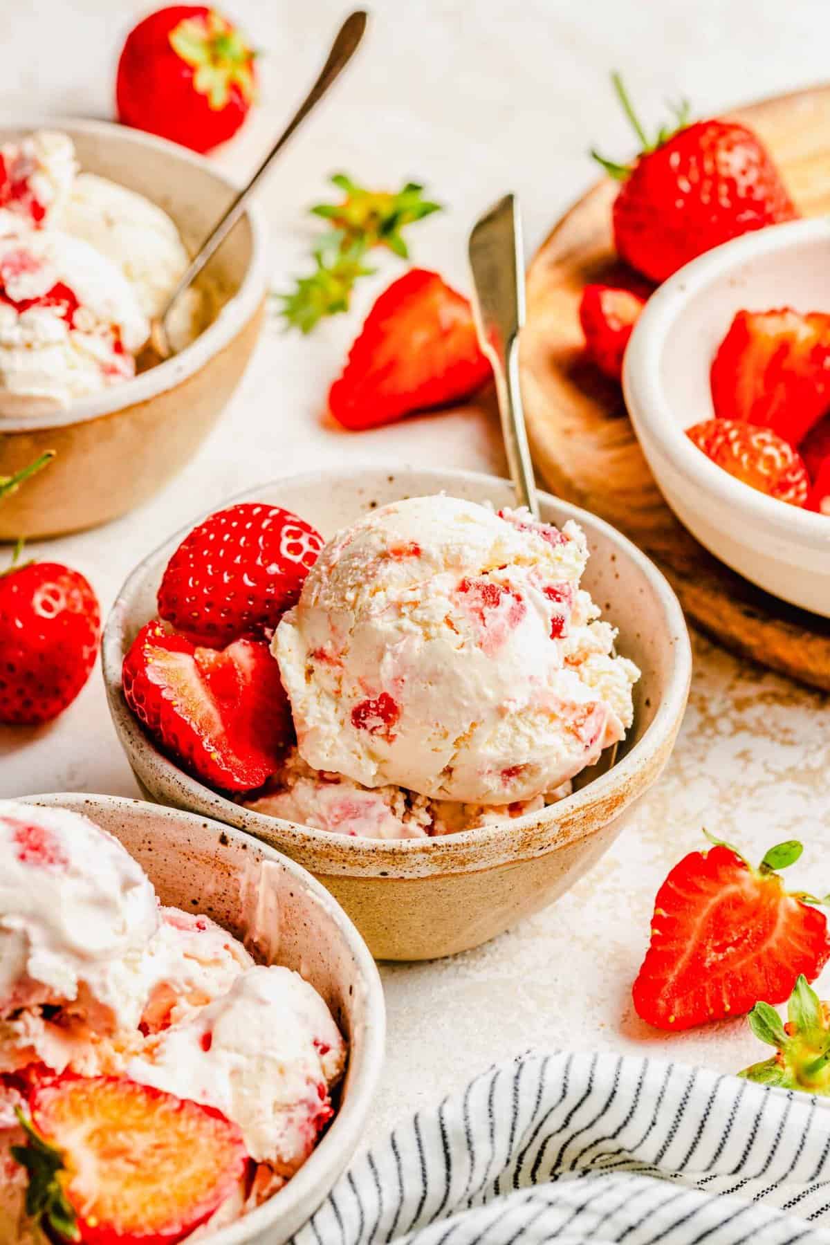 Strawberry ice cream served in bowls with spoons and garnished with fresh strawberries.