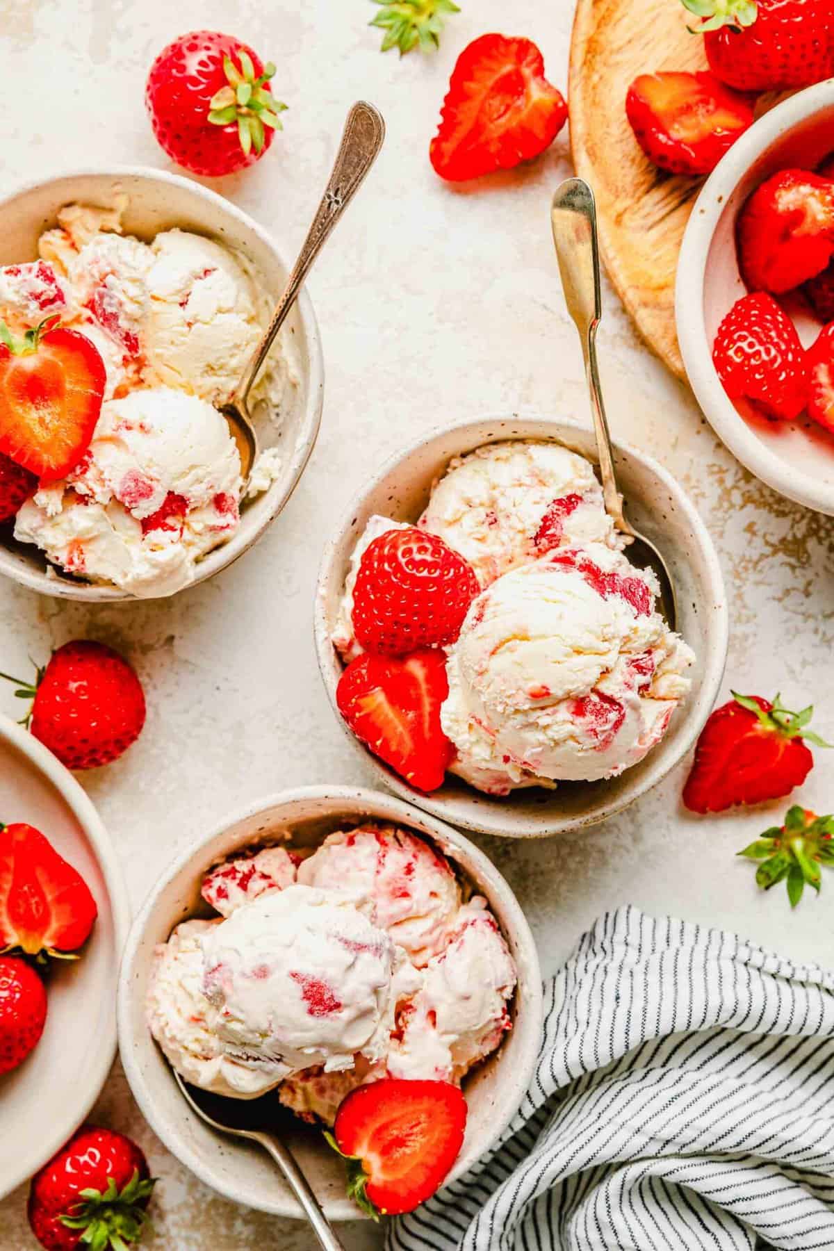 Overhead of strawberry ice cream served in bowls with spoons and garnished with fresh strawberries.
