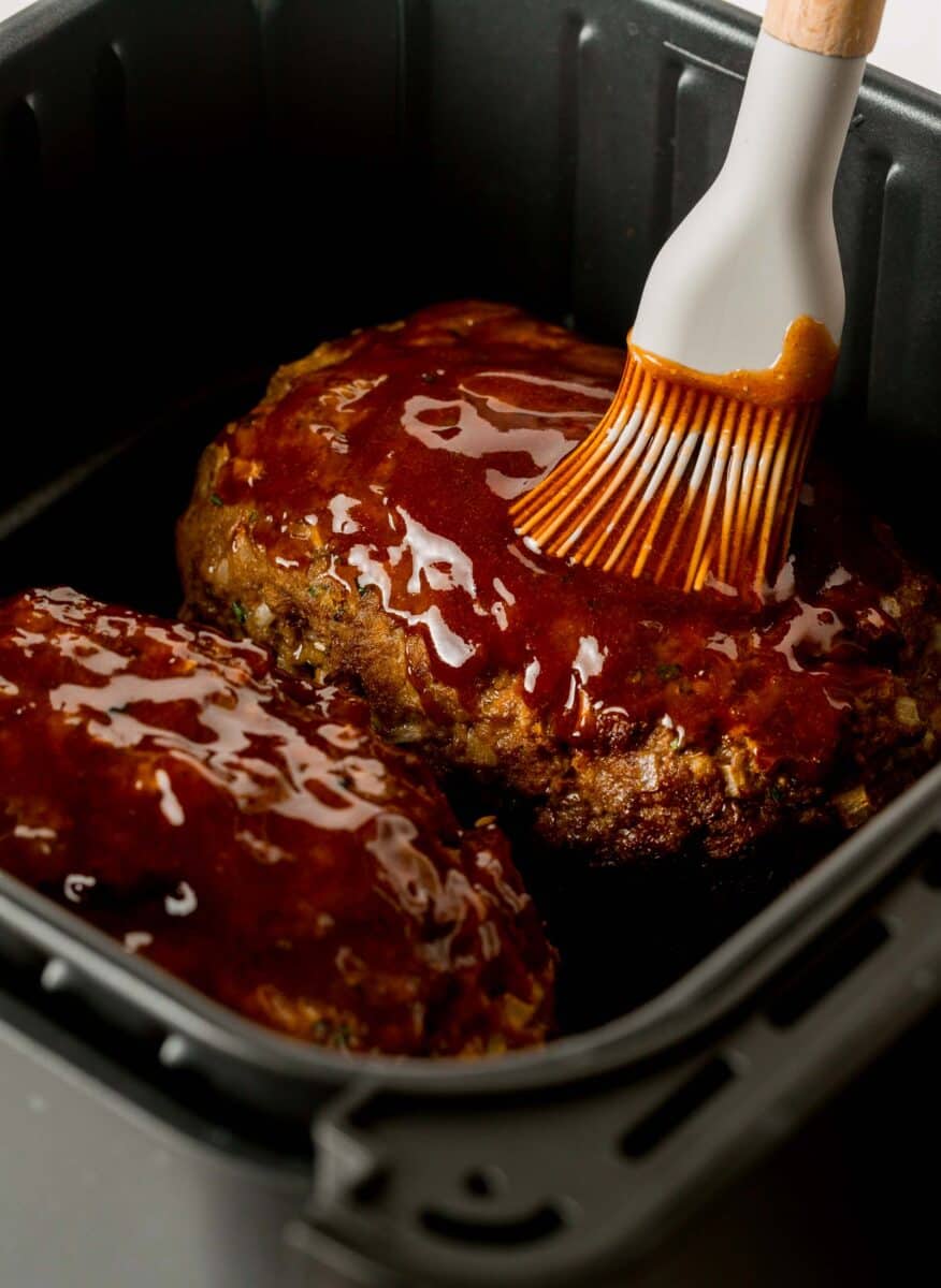 a silicone brush brushes meatloaf with meatloaf glaze mixture