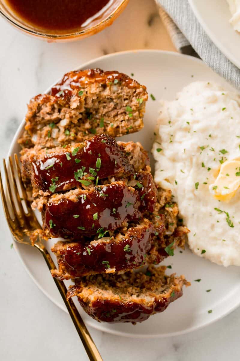 overhead image of meatloaf slices with fresh parsley sprinkled on top next to a mound of mashed potatoes