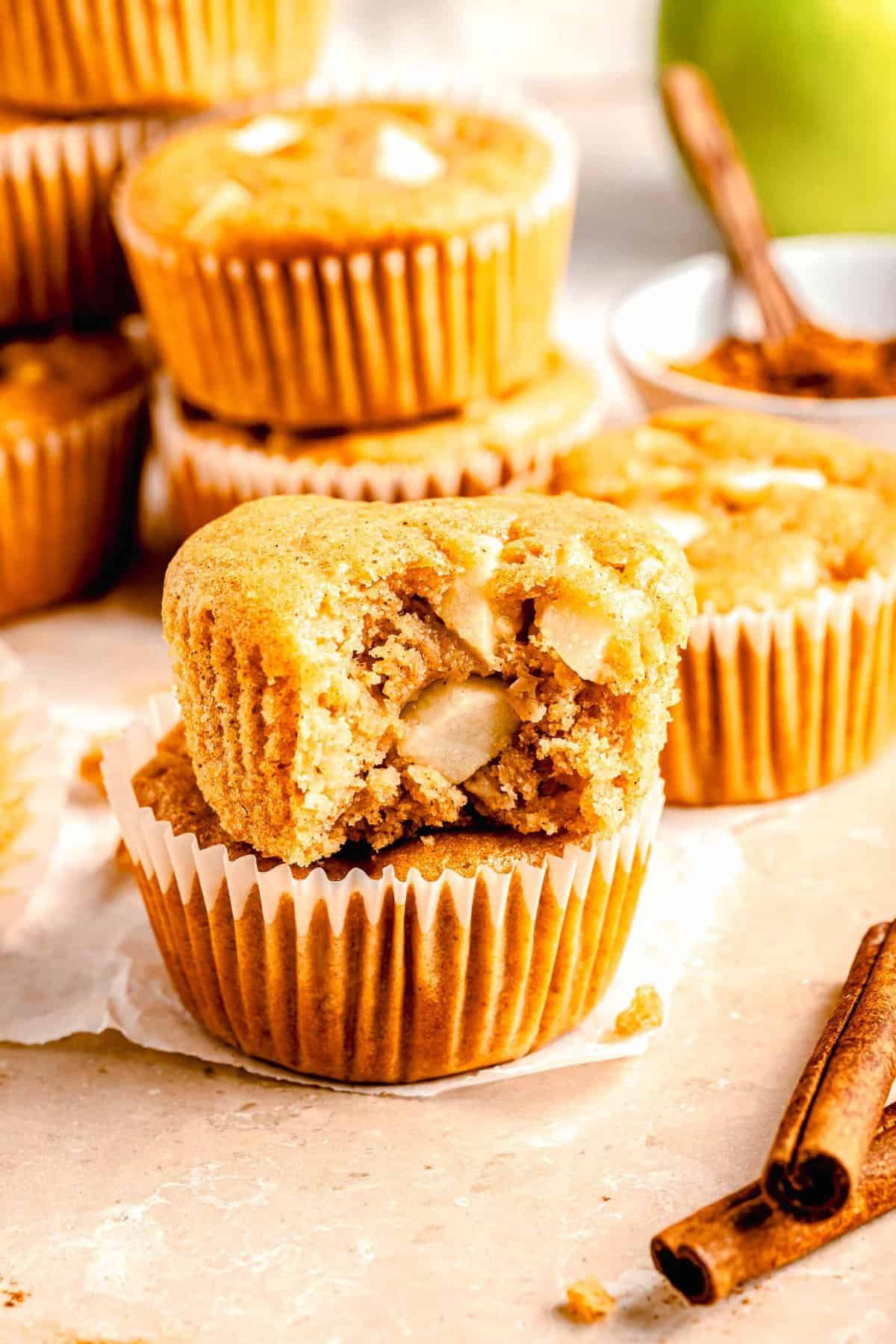 Apple cinnamon muffins stacked on top of each other. One of them has a bite taken out of it.