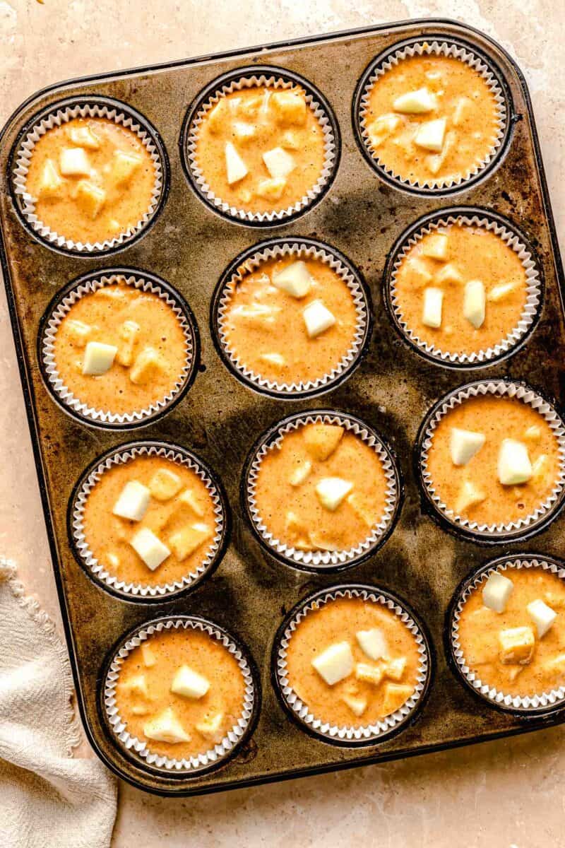 Muffin tins filled with cinnamon apple muffin batter.