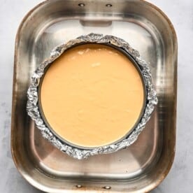 biscoff cheesecake mixture in a springform pan with foil wrapped around and in a large pan with water