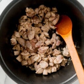 browning and cooking the cubed chicken thighs in a large dutch oven with a wooden spoon