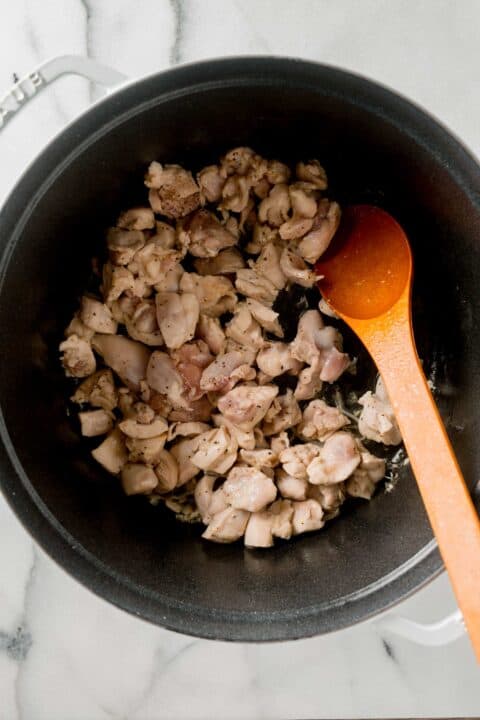 browning and cooking the cubed chicken thighs in a large dutch oven with a wooden spoon