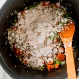 flour sprinkled on top of the vegetable mixture and wooden spoon in the dutch oven