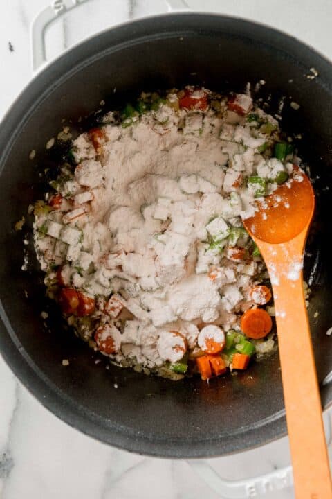 flour sprinkled on top of the vegetable mixture and wooden spoon in the dutch oven