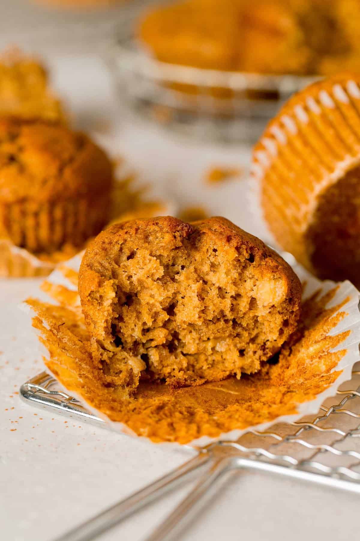 A partially unwrapped pumpkin banana muffins with a bite missing, revealing the fluffy, moist interior.