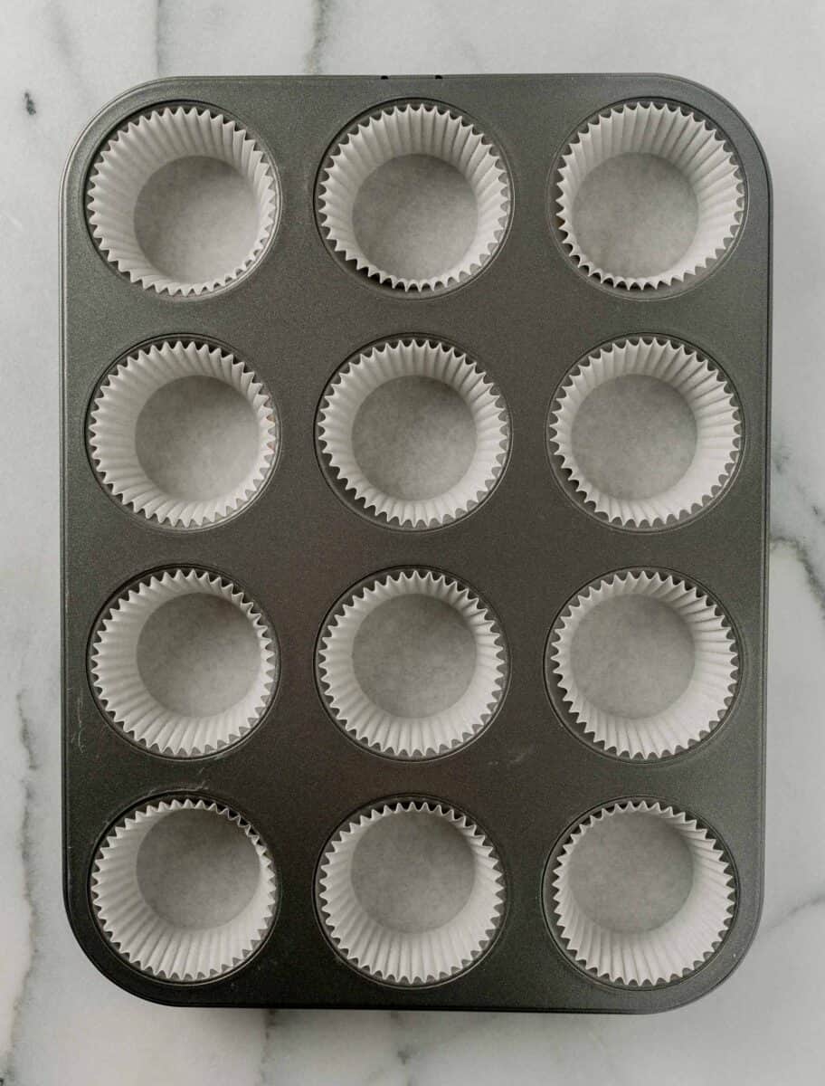 A 12-well metal muffin pan lined with paper muffin cups.