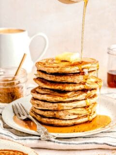 Pouring maple syrup over a stack of pumpkin spice pancakes.