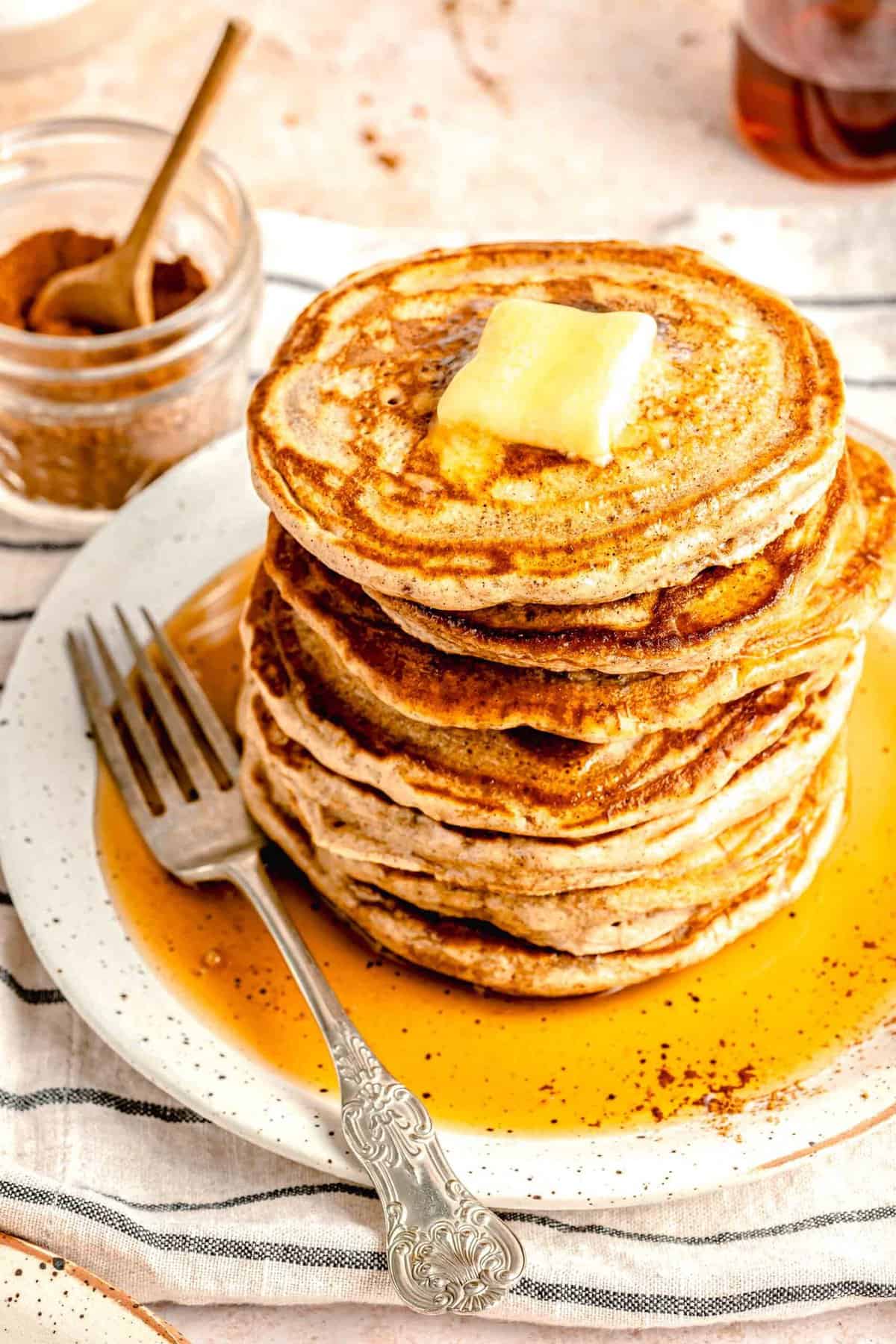 Overhead shot of a stack of pumpkin spice pancakes on a plate topped with butter and dowsed in maple syrup.