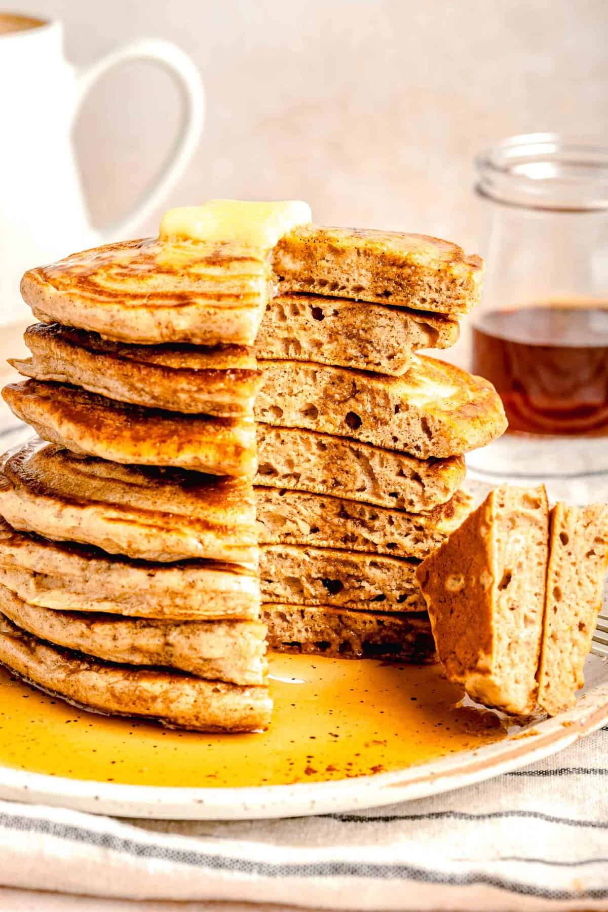 A stack of pumpkin spice pancakes with a slice taken out of it on a plate topped with butter and dowsed in maple syrup.