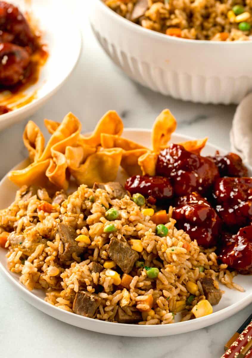 a plate of steak fried rice, general tso's chicken, and fried wontons