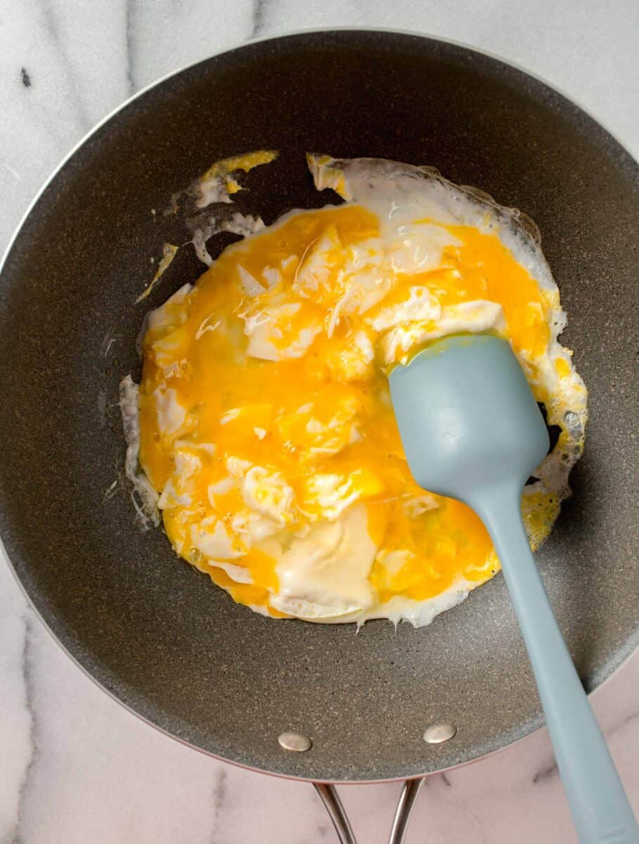 half cooked eggs in a large wok with a blue silicone spatula