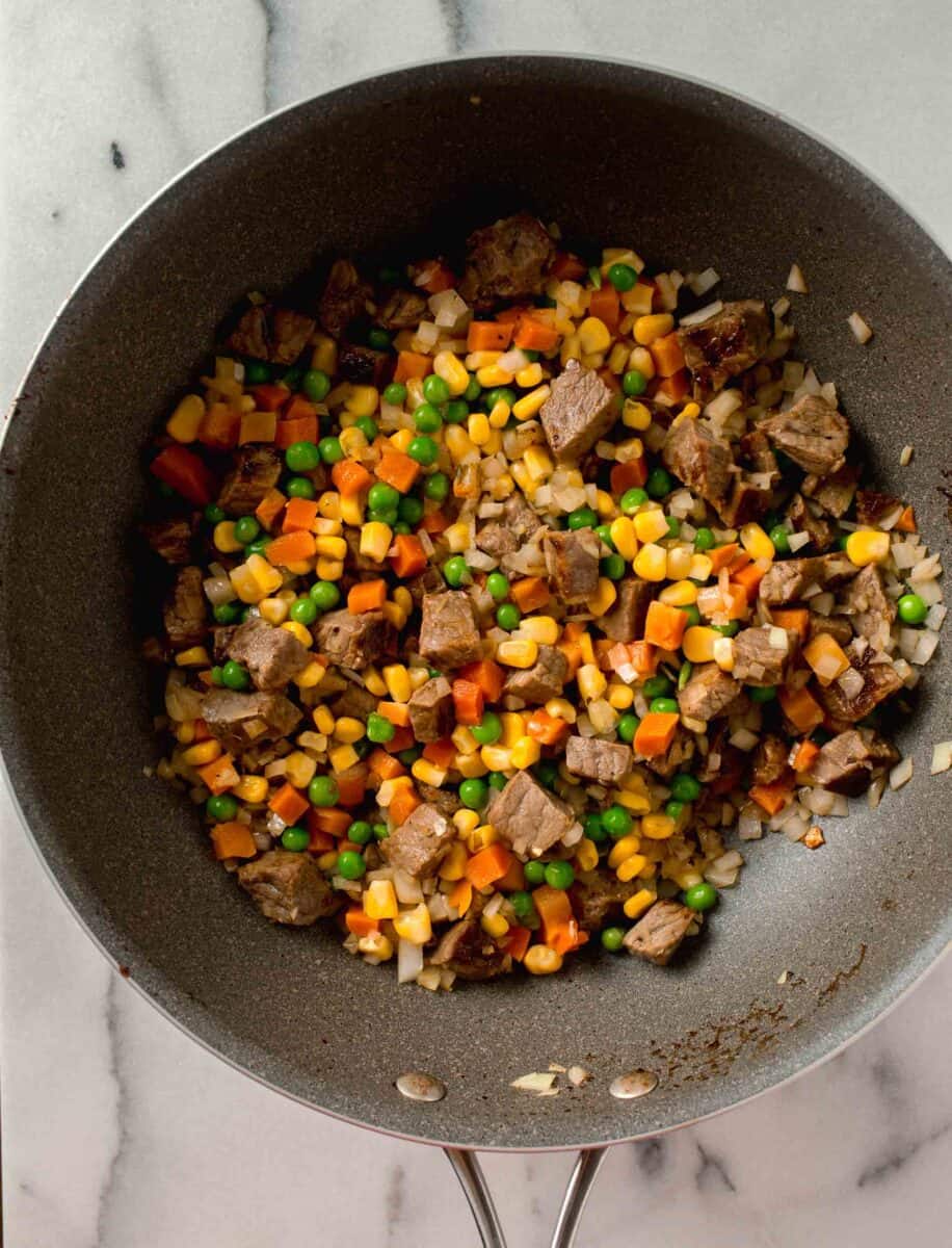 a medley of vegetables like carrots, peas, and corn are added to the wok with the cubed steak