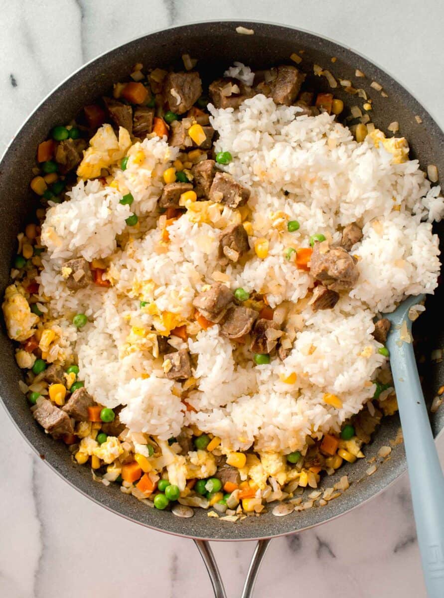 white rice added into the wok with the rest of the steak fried rice ingredients