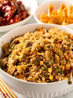 a large bowl of steak fried rice next to fried wontons and wooden chopsticks