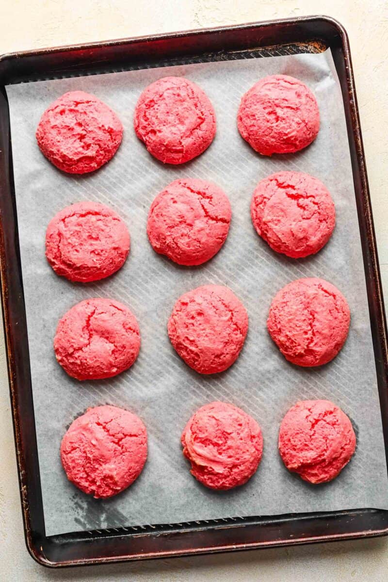 baked strawberry cream cheese cookies on parchment paper and a metal baking sheet