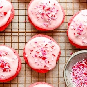 decorated strawberry cream cheese cookies on a wire cooling rack with valentine's day sprinkles on top