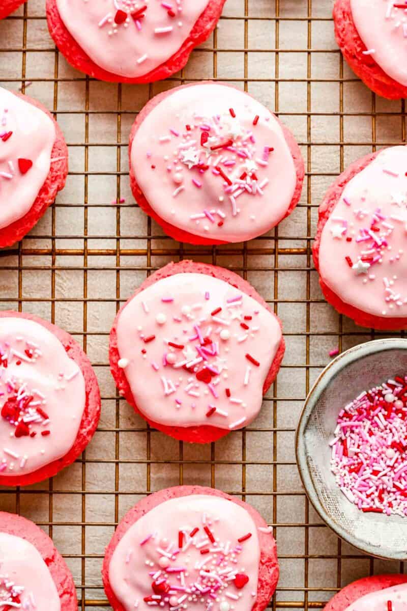 decorated strawberry cream cheese cookies on a wire cooling rack with valentine's day sprinkles on top