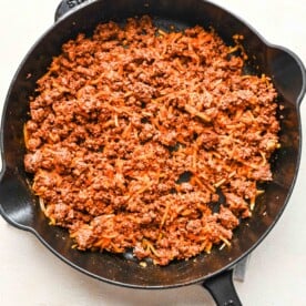 ground beef in a cast iron skillet with shredded cheese added to it