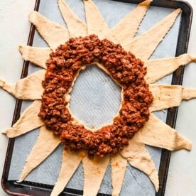 seasoned and cooked ground beef arranged in a circle on top of the crescent dough on a metal baking sheet